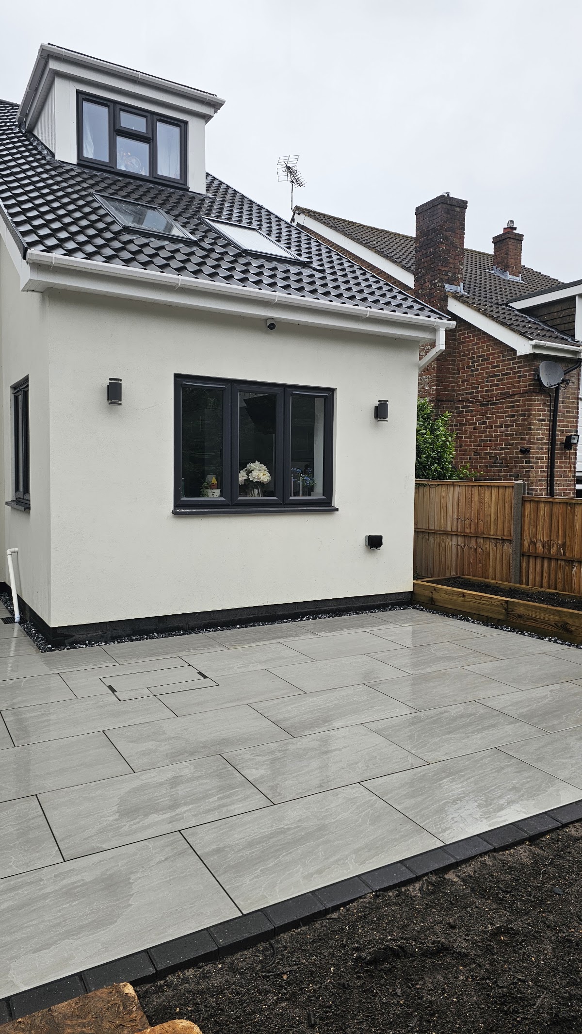 Large grey porcelain patio with charcoal edging beside a rendered house